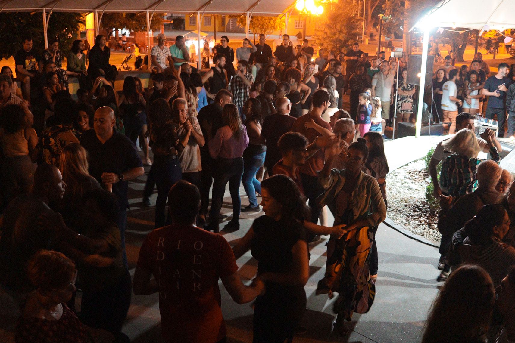 Plateia dançando forró sob a tenda na praça