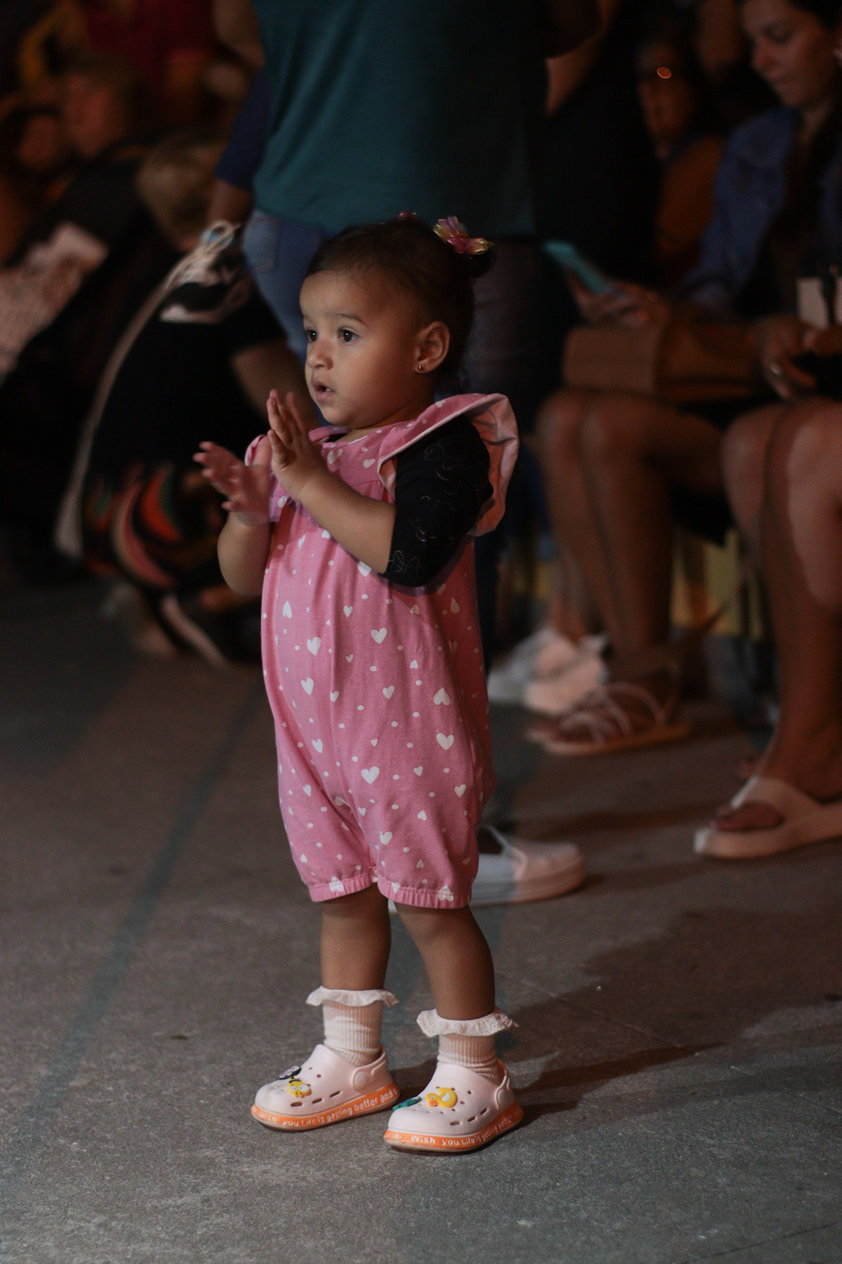 Bebê de macacão rosa batendo palmas para a banda